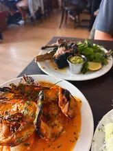 A close-up, top-down shot of a restaurant table featuring a plate of prawns in a vibrant sauce in the foreground and lamb chops in the background.
