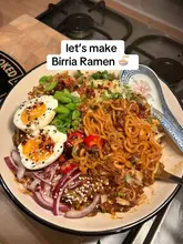 A top-down, appetising shot of a homemade bowl of Birria Ramen, featuring rich noodles, tender beef, soft-boiled eggs, and fresh garnishes, set against a standard home kitchen background.