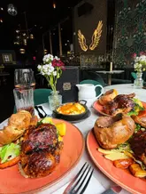 A high-quality, well-composed overhead shot of a Sunday roast spread at a restaurant. The image captures the meal clearly, with good lighting that highlights the texture of the roast chicken and the golden brown of the Yorkshire puddings, making the food look very appealing.