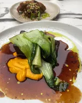 A close-up, top-down shot of a soy-braised short rib dish served with grilled pak choi and a beef stock glaze, captured at a restaurant in Newcastle.