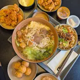 An overhead flat-lay shot of a Chinese restaurant spread featuring beef rice noodles, beef tripe, fried chicken, and sesame balls on a dark table.