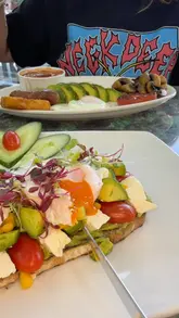 A vlog-style review of The Moon Cafe in Cardiff, featuring the creators trying various brunch items, including avocado toast, a breakfast plate, a strawberry coffee, a chocolate milkshake, and baklava.