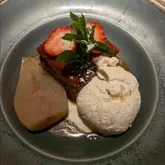 A close-up, overhead shot of a plated dessert featuring a slice of cake, a scoop of vanilla ice cream, a poached pear, and a strawberry garnish.