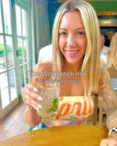 A bright, high-quality selfie-style shot of a creator holding a cocktail at The Woolpack Inn, featuring natural lighting and a pleasant, inviting atmosphere.