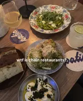 A flat-lay shot of a dinner spread featuring pasta, bread, a dip, and drinks, likely at an independent restaurant in Brighton. The image captures a casual dining experience with a focus on supporting local businesses over chains.