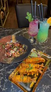 A montage-style video showcasing the food, drinks, and interior of Indara restaurant. The video features close-ups of various dishes like chaat, prawn tempura, a large mixed grill platter, and desserts, interspersed with shots of the restaurant's decor, including a large chandelier.