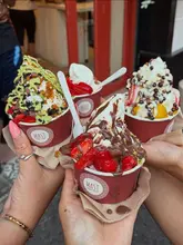 A bright, inviting shot of three cups of frozen yogurt held together in a 'cheers' formation, showcasing the variety of toppings available at the venue.