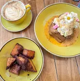 A top-down, overhead shot of a brunch spread featuring a plate of rhubarb and custard French toast, a side of crispy hash browns, and a latte on a wooden table.
