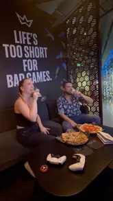 The video features a couple visiting XP Tavern, a gaming-themed bar. It highlights the atmosphere, the food (specifically pizzas), and the gaming experience, showing them enjoying drinks and playing on a PlayStation 5.