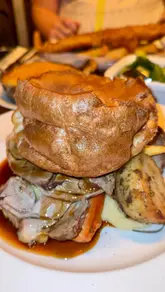 A montage video showcasing the Sunday lunch menu and interior of The Woodmans Arms, featuring various roast dinners, fish and chips, and desserts.