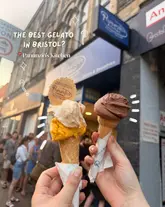 A first-person perspective shot of two gelato cones held up in front of a busy street scene, promoting Panunzio's Kitchen in Bristol. The image effectively highlights the product against a blurred background, creating a classic 'foodie' aesthetic.