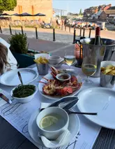 A high-quality, well-composed shot of a seafood dinner at a waterside restaurant. The golden hour lighting enhances the appeal of the lobster and wine, creating an inviting atmosphere that effectively communicates the dining experience.