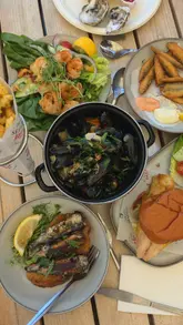 A montage showcasing a seafood feast at Osborne Bros in Leigh-on-Sea, featuring various dishes like oysters, mussels, and grilled sardines, set against a waterside backdrop.