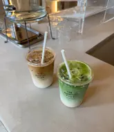 A clean, well-lit, and aesthetically pleasing shot of an iced latte and an iced matcha latte placed on a neutral counter, clearly branding the venue 'The Florist Files'.