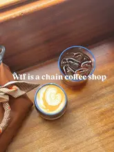 A simple, overhead shot of two coffee drinks—a latte with latte art and an iced coffee—placed on a wooden table next to a handbag. The image is clean, well-lit, and captures a casual coffee shop moment.