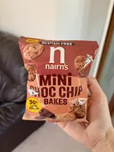 A casual, first-person snapshot of a packet of Nairn's Mini Choc Chip Bakes being held in a domestic setting.