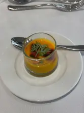 A close-up shot of an amuse bouche, specifically a chilled carrot soup, served in a small glass on a white tablecloth at the Genesis Scottish Open, prepared by chef Tom Kitchin.