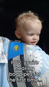 A short, handheld video capturing a baby's reaction to hearing bagpipes for the first time while visiting Stirling Castle. The footage includes a brief shot of a pipe band performing in the castle courtyard.