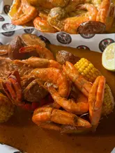 A close-up, top-down shot of a seafood boil served on paper, featuring shrimp, corn, and potatoes covered in a thick sauce.