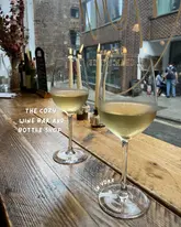 A cozy, atmospheric shot of two glasses of white wine placed on a rustic wooden bar counter in front of a window, capturing the relaxed vibe of a wine bar in York.