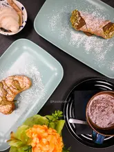 A high-quality flat-lay photograph showcasing a selection of Italian pastries and a hot chocolate from a cafe, arranged neatly on a dark surface.