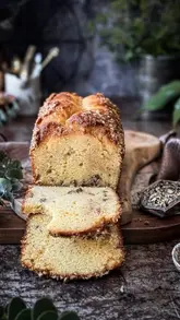 A high-quality, moody food photography shot of a maple walnut loaf cake, sliced to reveal its texture. The image uses dramatic, low-key lighting to highlight the moist crumb and crunchy walnut topping, creating an inviting and rustic aesthetic suitable for a baking blog or social media post.