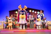 A high-quality promotional photograph for the 'Bluey's Big Party' stage show, capturing the costumed characters and performers on a brightly lit theatre set.