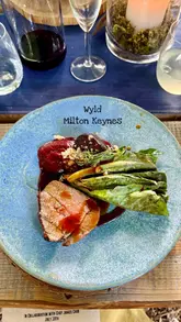 A montage-style video showcasing a woodland dining event featuring live-fire cooking, a set tasting menu, and an outdoor, nature-focused atmosphere.