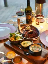 A high-quality, atmospheric shot of a tomahawk steak dinner served with wine, showcasing a premium dining experience.