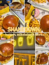 A collage-style promotional image for Shakedown, showcasing various menu items including burgers, wings, and mozzarella dippers, alongside a glimpse of the venue's interior seating and neon signage.