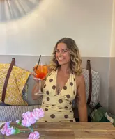 A lifestyle-focused promotional shot featuring a smiling woman holding an Aperol Spritz in a restaurant setting, intended to convey a relaxed and inviting atmosphere.