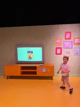 A photo of a young child standing in a themed Peppa Pig room, likely at an interactive attraction, capturing the immersive set design.