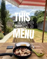A 45-degree shot of a pan containing a shakshuka-style dish with eggs, chorizo, and feta, set on a wooden table in a garden. The image is heavily overlaid with large white text reading 'THIS WEEK'S MENU'.