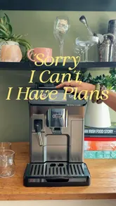 A short, aesthetic video demonstrating the use of a De'Longhi Eletta Explore coffee machine at home, showing the process of making an iced coffee and enjoying it on a patio.