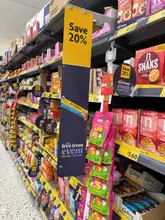 A promotional photograph taken inside a Morrisons supermarket aisle, highlighting a 'Free From' event with 20% off various gluten-free and plant-based snacks, including oatcakes, crackers, and sweets.