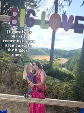 A candid, sunlit photograph of a mother and child embracing in front of a 'BIG LOVE' sign at a festival, set against a scenic backdrop of the Welsh countryside. The image captures a warm, family-oriented moment, using the festival signage to frame the subjects.