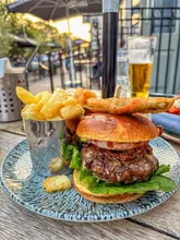 A high-quality, well-lit shot of a pub-style beef burger served with chips, captured during golden hour on an outdoor terrace. The image effectively conveys a relaxed, enjoyable dining experience.
