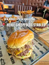 A close-up shot of two smash burgers and fries served on metal trays at a restaurant called Herd, featuring branded paper.