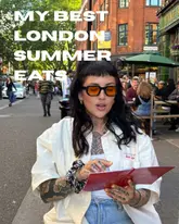 A creator sits at an outdoor table on a busy London street, holding a notebook and introducing a list of summer food recommendations.
