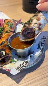 A close-up, action-oriented shot of a hand dipping a kofta-style wrap into a sauce, effectively highlighting the texture and appeal of the food.