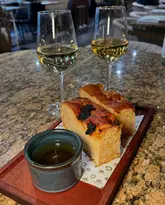 A close-up shot of a starter course consisting of focaccia bread served with a dipping oil, accompanied by two glasses of white wine on a marble table at a restaurant.