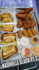 A food review video featuring two men in a car trying various menu items from The Nashville Cluck, including cheese bites, chicken tenders, and burgers.