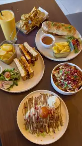 A flat-lay photograph showcasing a variety of desi fusion dishes, including a nihari sub, keema sando, samosa chaat, pakoras, and a gulab jamun croissant, arranged on a dark table.
