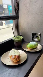 A short, aesthetic promotional video for a new Korean cafe in Soho called Tokkia, highlighting their signature salt bread pastries and matcha drinks, including a unique serving window feature.