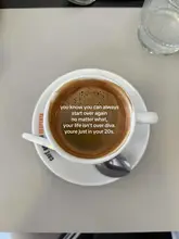 A simple, overhead shot of a cup of coffee on a saucer, featuring an inspirational text overlay.