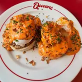 A high-quality, overhead food shot of a fried chicken eggs benedict dish with buffalo hollandaise sauce, served on a branded plate at a diner.