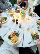 A group brunch scene at 1 Lombard Street, featuring a table spread with lobster rolls, steak and eggs, fries, and various drinks. The image captures a social dining experience with a focus on the table setting.