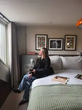 A high-quality, well-composed lifestyle shot featuring a person sitting on a hotel bed, looking out of a window in a bright, modern room.