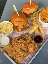 A high-angle shot of a casual meal served on a branded tray, featuring two burgers, a side of mac and cheese, fries, and breaded chicken tenders.