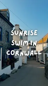 A serene, early-morning shot of a quiet street in Port Isaac, Cornwall, capturing the peaceful atmosphere of a sunrise swim. The composition effectively uses the leading lines of the street to draw the viewer into the scene, while the soft, golden-hour lighting enhances the charm of the coastal village.